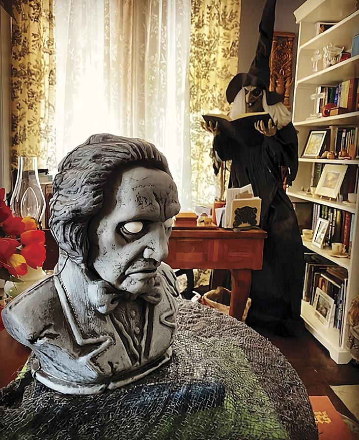 a ghoulish bust sit on a side table while a witch reads a spellbook in the background