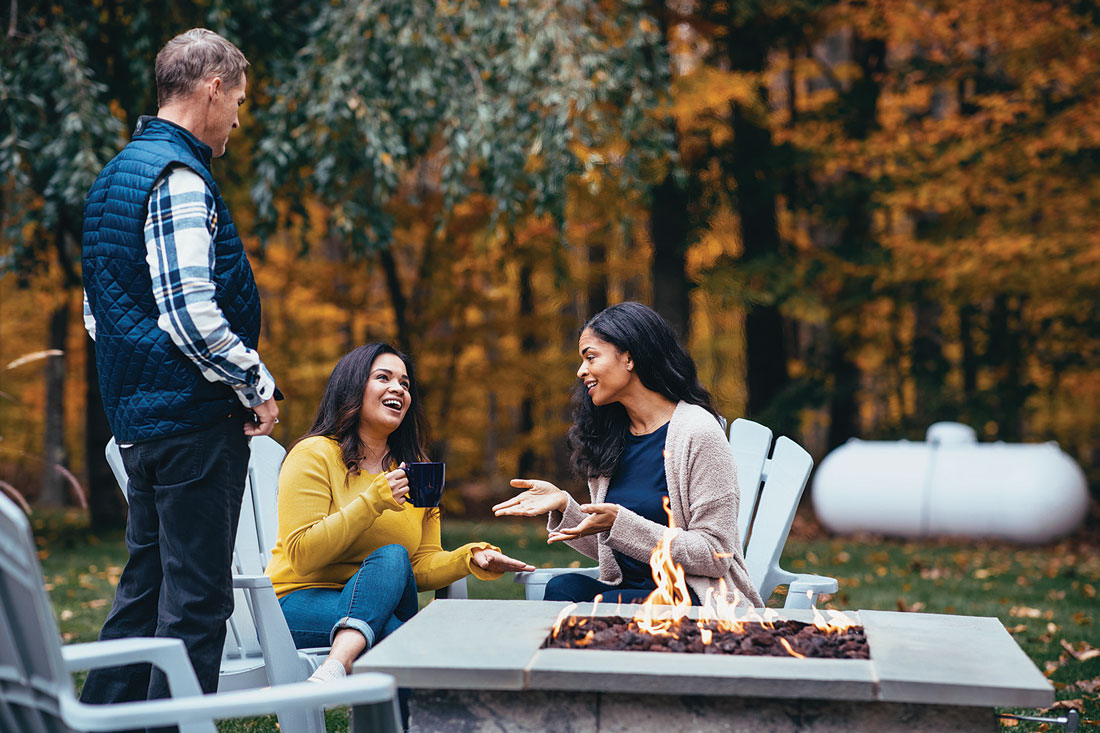 three people socializing around a propane-fueled fire pit